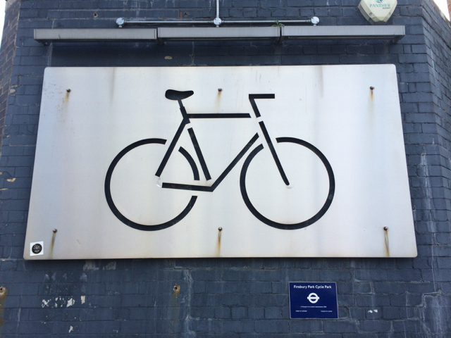 Metal panel with silhouette of bicycle frame cut into it mounted on a purple brick wall