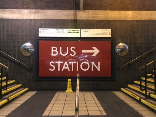 Large red sign with white text saying 'bus station' with a big arrow pointing right. What the picture shows is how massive this sign is compared to much smaller signs above that show the bus station can be reached in both directions