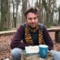 Photo shows Oliver Broadbent sitting with his notebook in a forest.