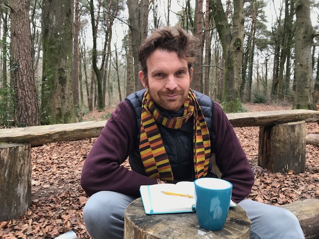 Photo shows Oliver Broadbent sitting with his notebook in a forest.